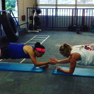 Two women are doing plank exercises in a gym.